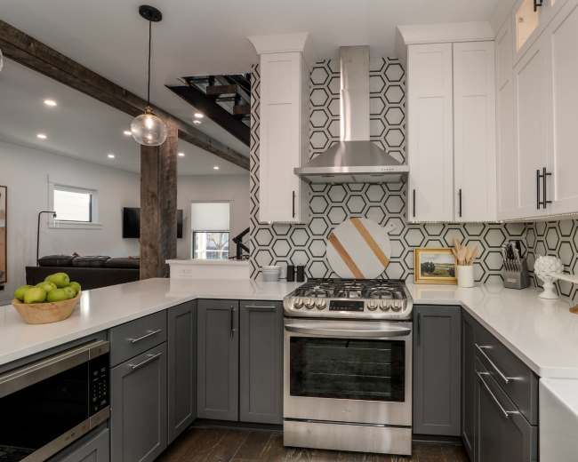 A modern kitchen features gray and white cabinetry, a stainless steel stove, and a geometric tile backsplash.