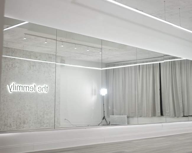 A bright, minimalistic room features a large mirror and soft curtains, with a neon sign that reads "the family."