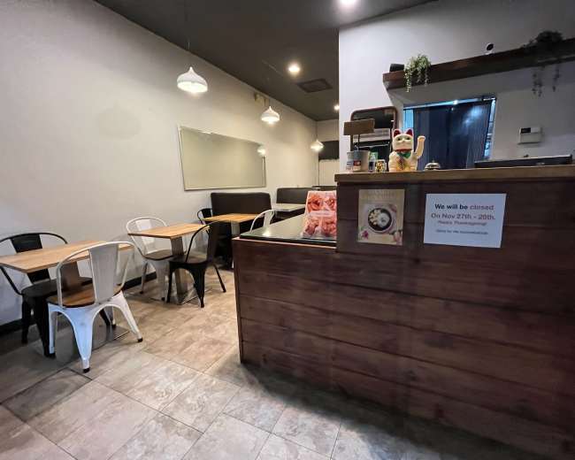 The image shows a small café interior with wooden counters, several tables, and a sign indicating the café will be closed on specific dates.