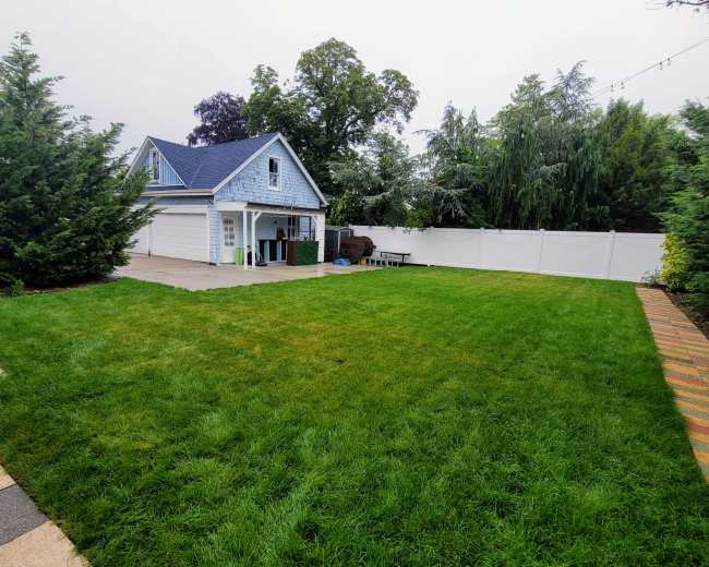 The image shows a spacious backyard with a well-manicured lawn, a small shed or garage, and a white fence lining the perimeter.