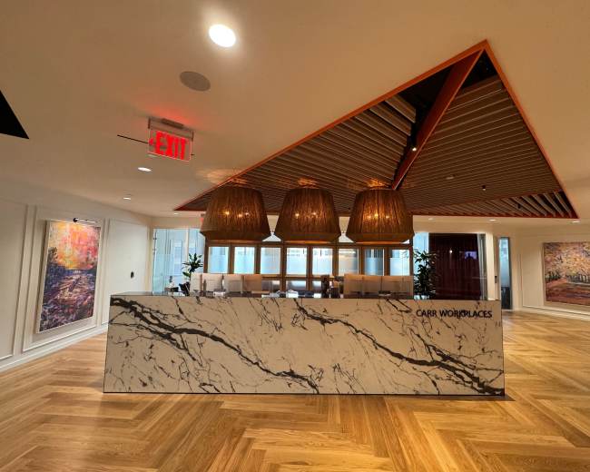 The image shows a modern reception area featuring a marble front desk, stylish light fixtures, and large artworks on the walls.