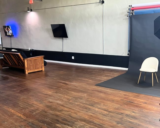 A spacious interior with a chair positioned in front of a black backdrop, accompanied by a lighting umbrella on a stand.