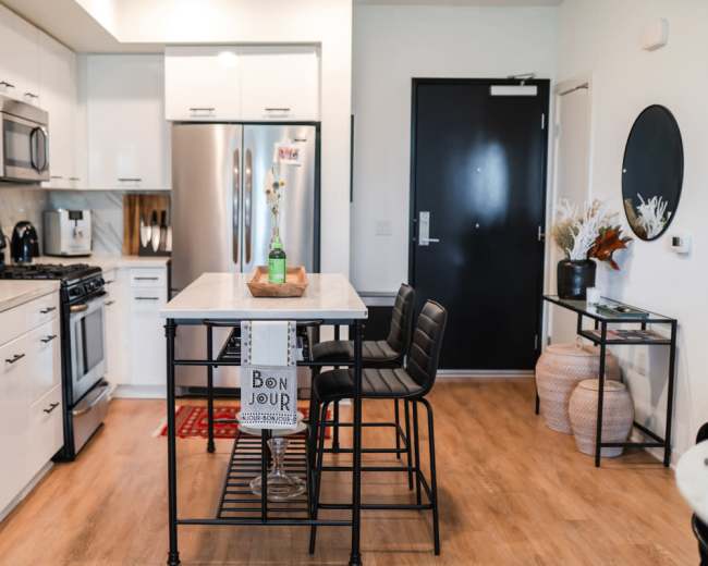 A modern kitchen features sleek white cabinets, stainless steel appliances, and a central island with bar stools.