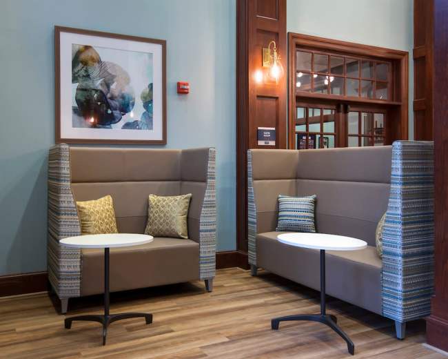 A cozy seating area with two upholstered booths, each paired with a small round table, set against a backdrop of wood paneling and an abstract artwork on the wall.