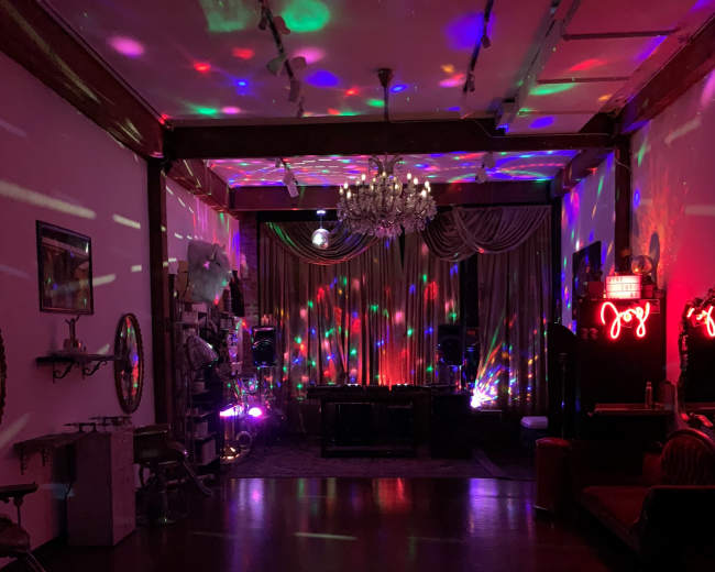 The room features colorful lights reflecting off the walls, a chandelier, and stylish furnishings.