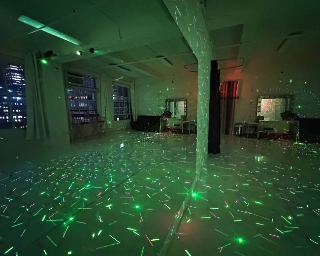 The room features a reflective floor illuminated by green and red laser light patterns against a dark background.