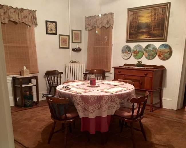 A cozy dining room with a round table set in the center, surrounded by wooden chairs, and adorned with framed artwork and decorative plates on the walls.