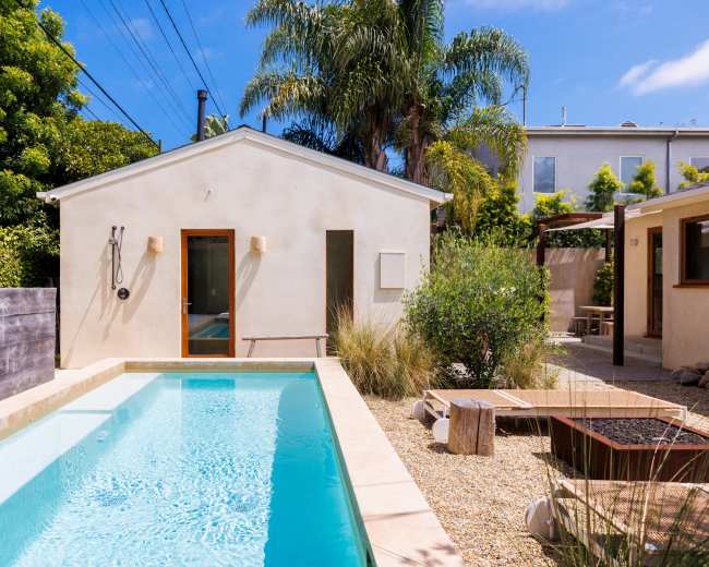 A modern backyard featuring a swimming pool alongside a small house, surrounded by greenery and outdoor seating areas.