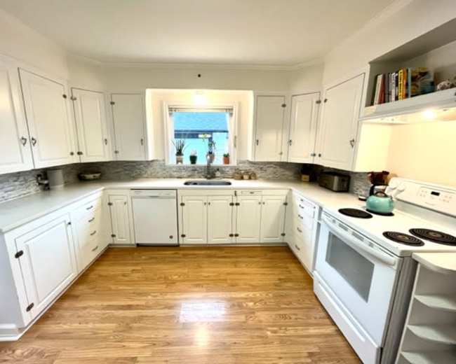 A well-organized kitchen features white cabinets, a gray countertop, and modern appliances surrounding a central window.
