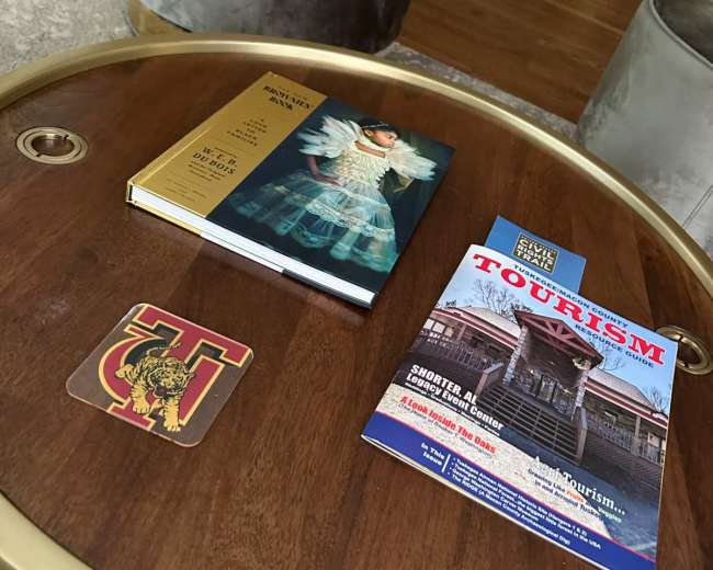 A wooden coffee table holds a book, a tourism magazine, and a coasters with the letter "T" and a lion emblem.