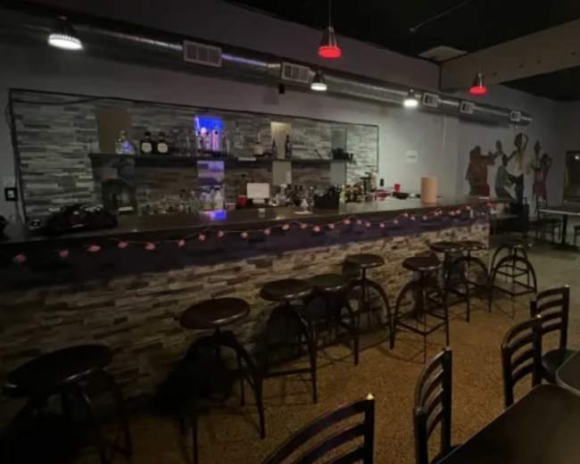 The image shows a dimly lit bar area with a stone countertop, several bar stools, and a pool table in the background.