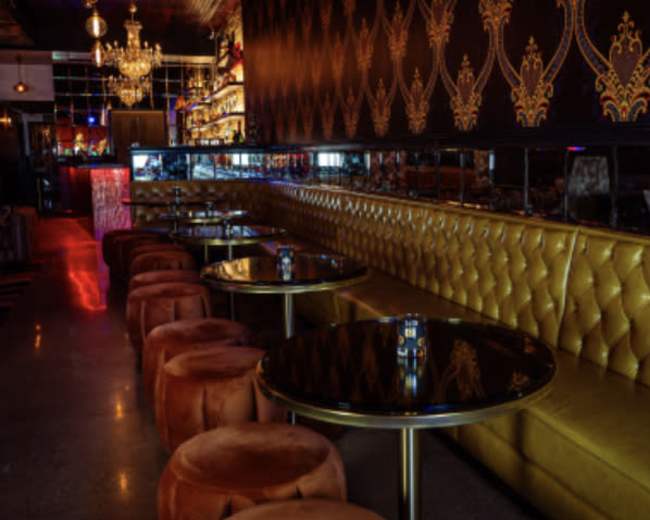 The image shows a stylish lounge with a golden tufted seating area, round tables, and ambient lighting.