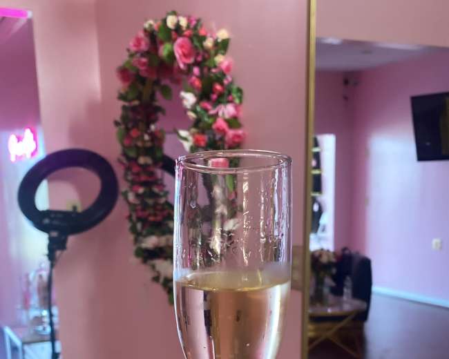 A person holds a clear champagne glass in front of a pink-walled room adorned with floral decorations.