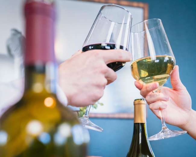 Two people clink glasses filled with red and white wine, with a J. Lohr wine bottle prominently displayed in the foreground.