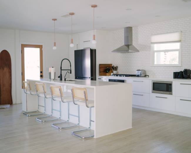 A modern kitchen features a large white island with bar stools, stainless steel appliances, and a wall of white brick.