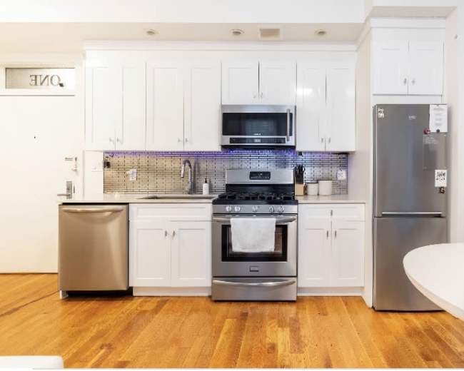 The kitchen features white cabinetry, stainless steel appliances, and wooden flooring.