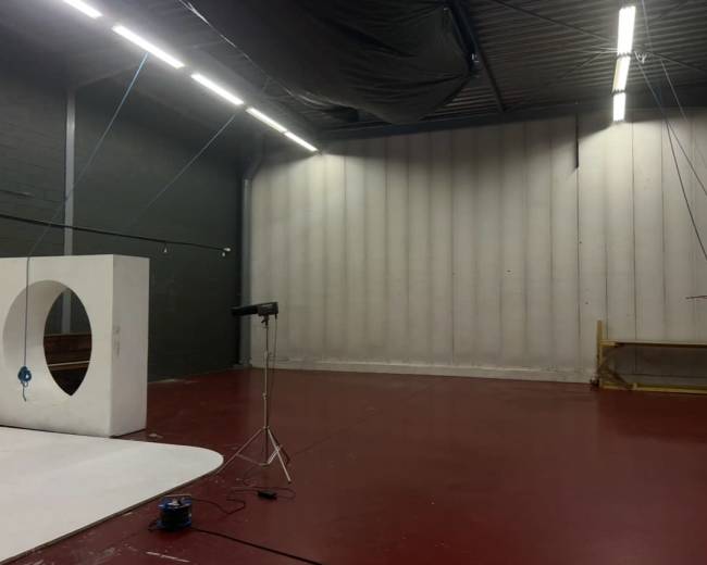 The image shows a spacious studio with a red floor, a large white backdrop, and a black cloth hanging from the ceiling.