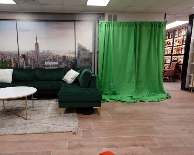 The scene features a green couch and a round white table on a rug, with a green backdrop to the right and a large cityscape mural on the wall behind.