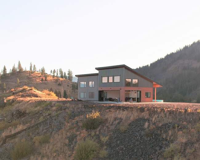 A modern house is situated on a hillside overlooking a mountainous landscape.