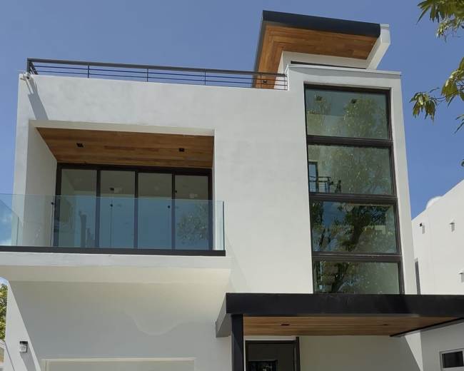 The image shows a modern, two-story house with large glass windows and a flat roof, accompanied by a black vehicle parked in front.