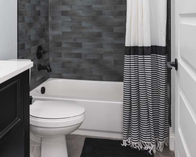A modern bathroom with a bathtub, a gray tiled shower area, a black and white striped shower curtain, and a black vanity.