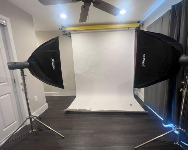 A photography studio setup with two softbox lights positioned on either side of a white backdrop.