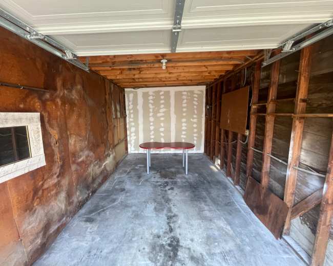 The image shows an empty garage with exposed walls, a concrete floor, and a small table in the center.