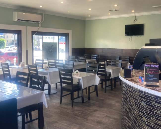 The image shows the interior of a restaurant with several tables set for dining and a service counter in the foreground.