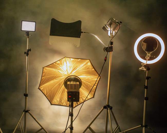A setup of various lighting equipment, including softboxes and ring lights, arranged on tripods against a backdrop.