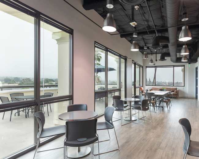 A modern indoor lounge area with tables and chairs, large windows, and a view of the outdoors.