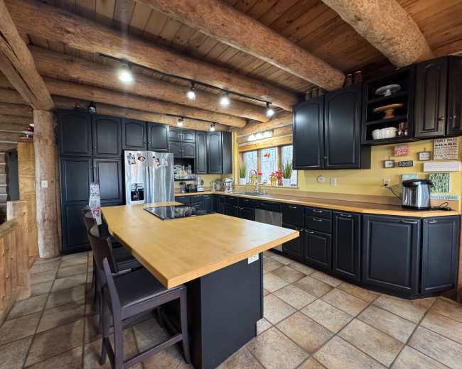 The kitchen features wooden beams overhead, black cabinetry, a central island with seating, and stainless steel appliances.