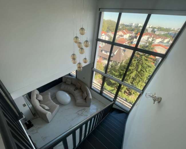The image shows a modern staircase leading down to a spacious living area with a rounded sofa and a large window overlooking a neighborhood.