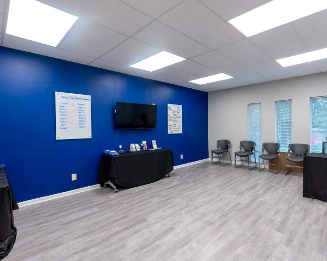 The image shows a large room with a blue accent wall, a television, several chairs, and tables displaying items along one side.