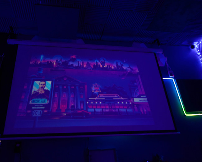 A colorful digital illustration is projected onto a screen, depicting a city skyline with futuristic buildings and neon elements.