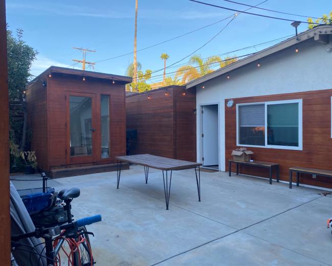 A courtyard with a wooden table, surrounded by buildings made of wood siding, and string lights overhead.