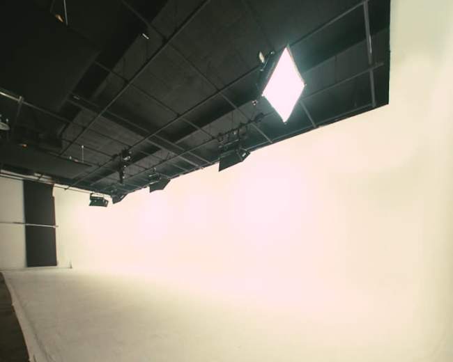 A spacious photography studio features a white backdrop and overhead lighting.