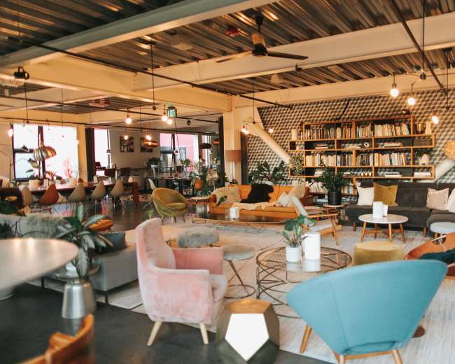 The image shows a modern, stylish lounge area with various seating options, plants, and decorative lighting.