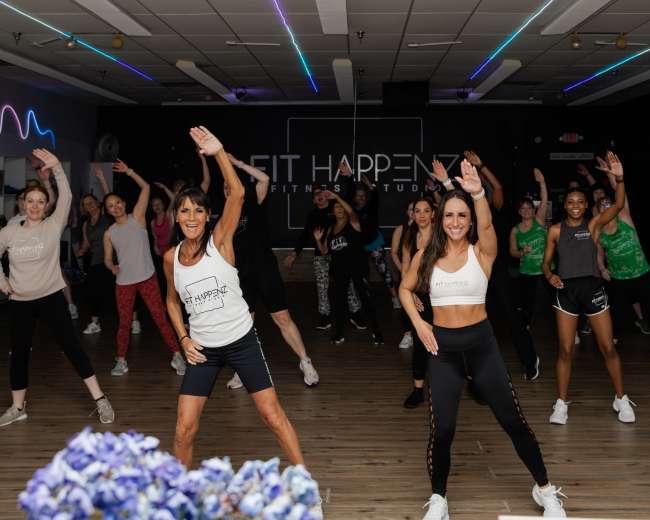 A group of people is participating in a fitness class at a studio, with some instructors leading the movements.