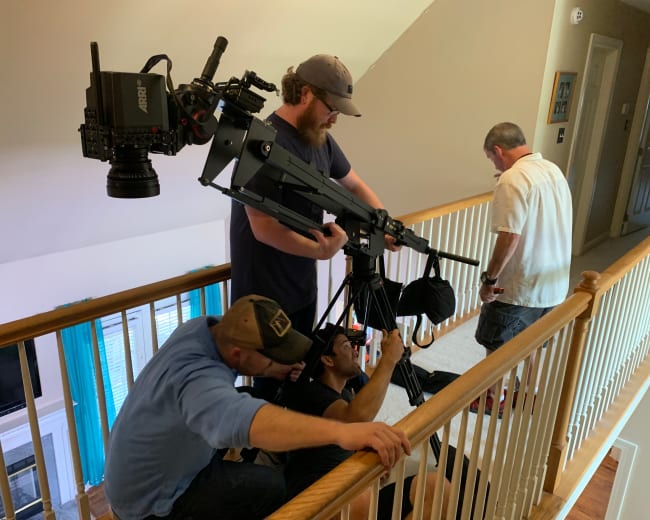 A group of four people sets up filming equipment on a staircase in a well-lit interior space.
