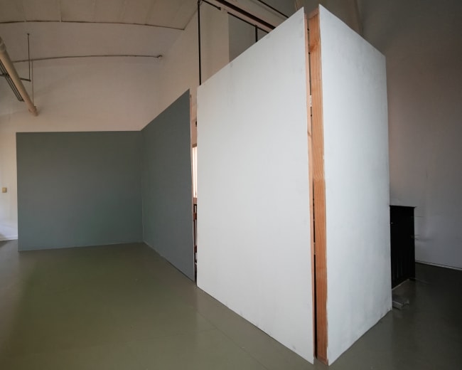 The image shows a spacious indoor area with plain walls and a distinct division created by a partition in the center.