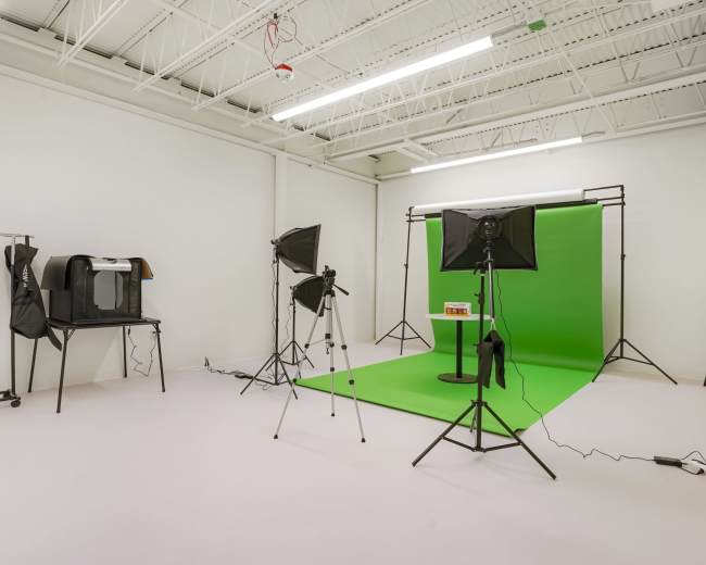 A photography studio with a green backdrop, lighting equipment, and a small table positioned in front of it.