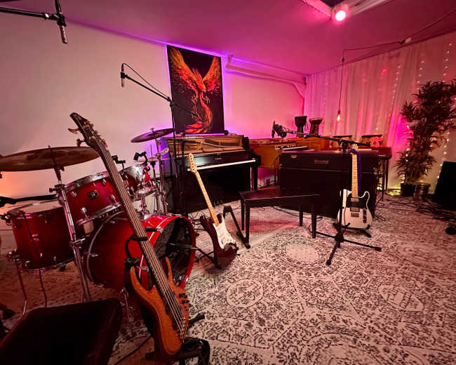 The image shows a music studio setup featuring various instruments, including a drum kit, acoustic and electric guitars, and a grand piano, with colorful lighting enhancing the ambiance.