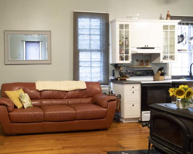 The image depicts a living room with a brown leather couch, a small coffee table with sunflowers, and a modern kitchen area visible in the background.