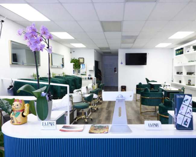 The image shows a modern salon interior with a reception area featuring a white counter, decorative plants, and green salon chairs in a tidy space.