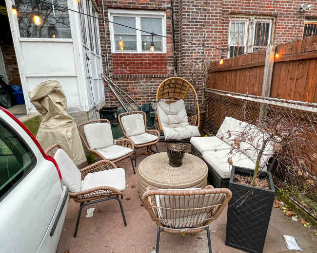 A cluster of outdoor furniture, including chairs and a table, is set up in a backyard surrounded by a wooden fence and brick walls.