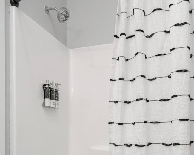 The image shows a simple bathroom with a shower curtain, a showerhead, and a bathtub.