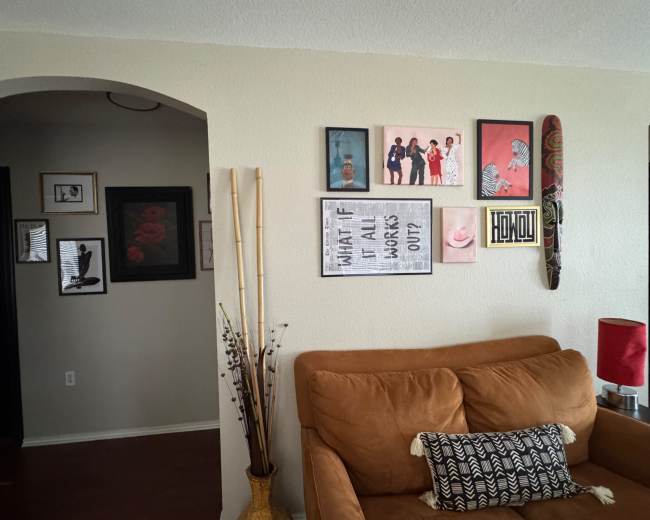 The scene shows a living room with a brown couch, framed wall art, decorative plants, and a red lamp.