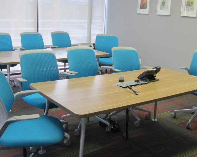 The image shows a conference room with multiple blue chairs arranged around wooden tables and a telephone on one of the tables.