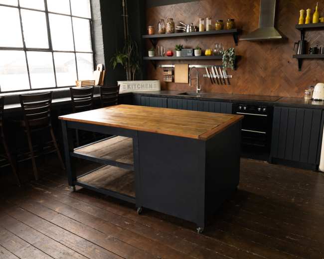 The image shows a modern kitchen featuring a wooden island with a dark base, black cabinets, and a vintage-style refrigerator, all set against a backdrop of a large window and wooden flooring.