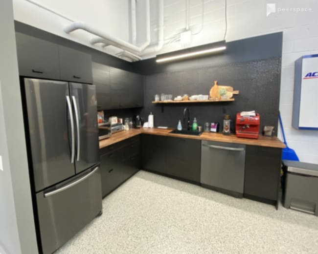 The image shows a modern kitchen with dark cabinets, a stainless steel refrigerator, a wooden countertop, and various kitchen appliances on a shelf against the wall.